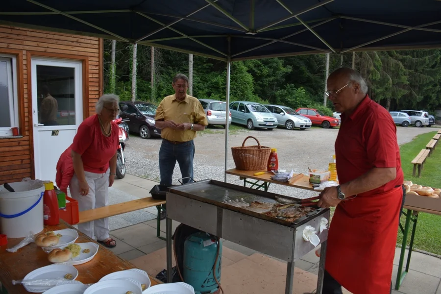 Seniorengrillmeister Pauli Aichholzer#nimmt den Grill in Betrieb#Die Obfrau und Seppi Wienerroither beobachten mit Sicherheitsabstand